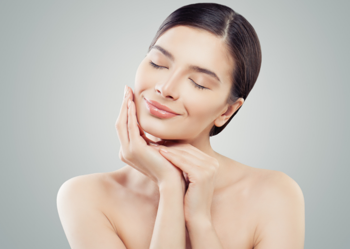 A woman with closed eyes, resting her chin on her hands, smiling with a serene expression, against a plain background, evokes the tranquility often found in a top-tier medical spa in Reno.