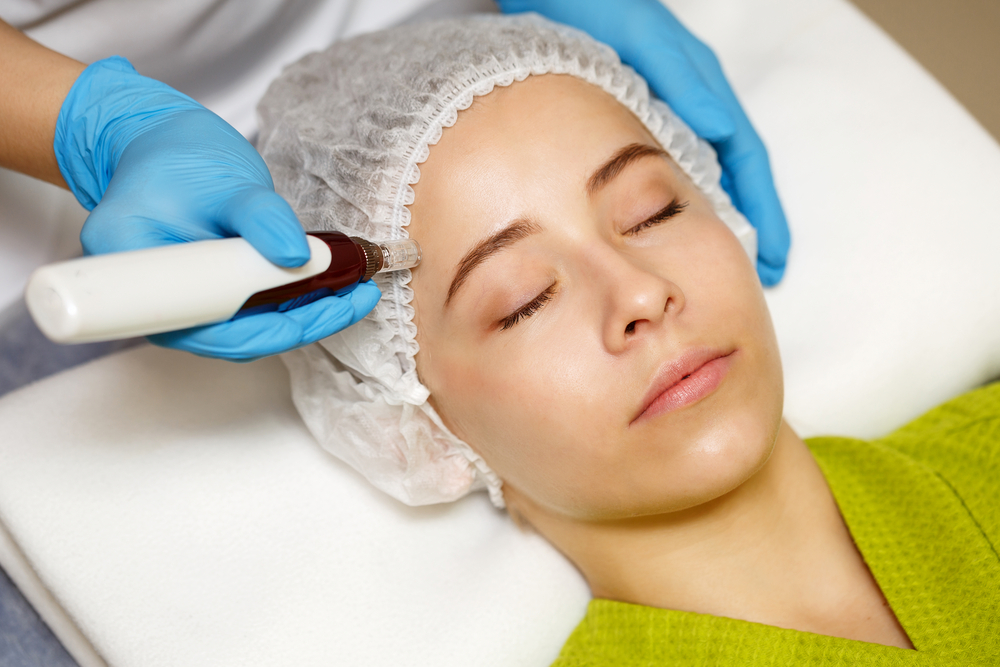 A person is lying down with closed eyes, wearing a hairnet and green garment, at a medical spa in Reno, Nevada, while another individual in blue gloves uses a handheld device on their forehead.