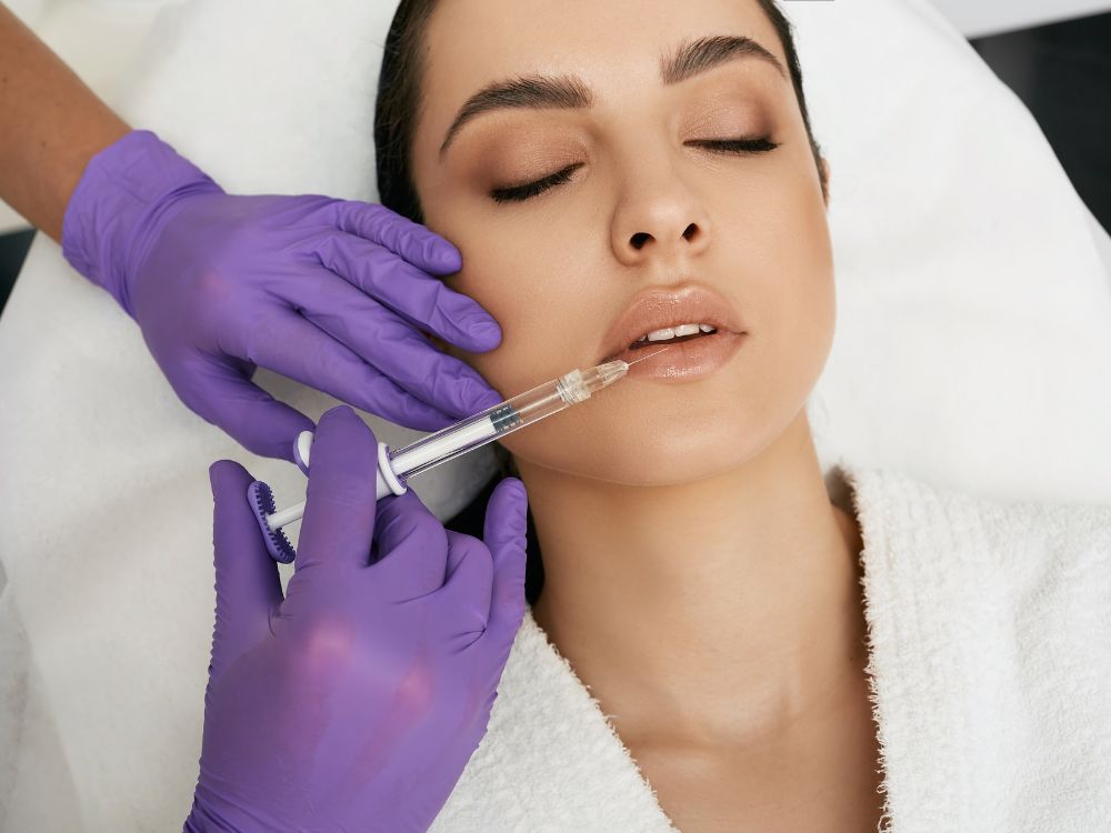 At a renowned aesthetics med spa, a person receives a cosmetic lip injection from a professional wearing purple gloves.