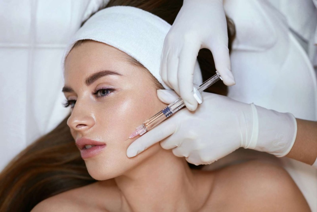 At a renowned aesthetics med spa, a person receives a cosmetic injection to the face from a gloved professional.