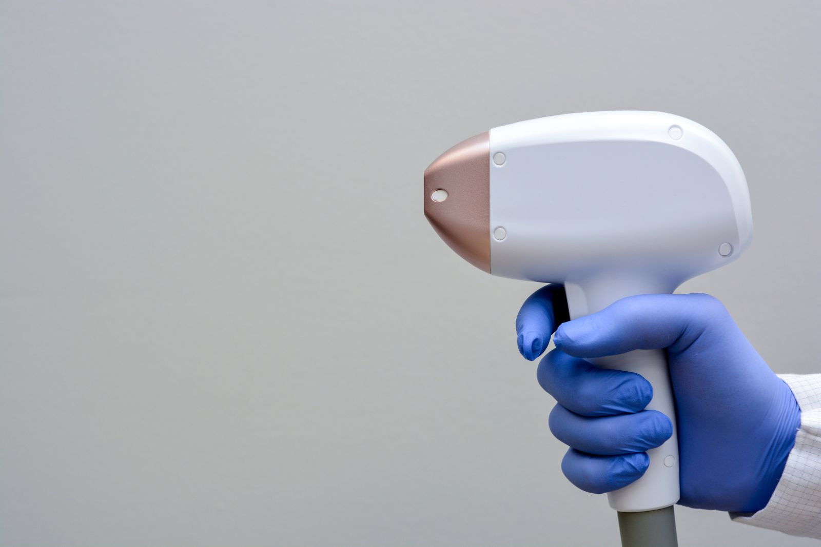 A person in blue gloves holding a hair removal device.