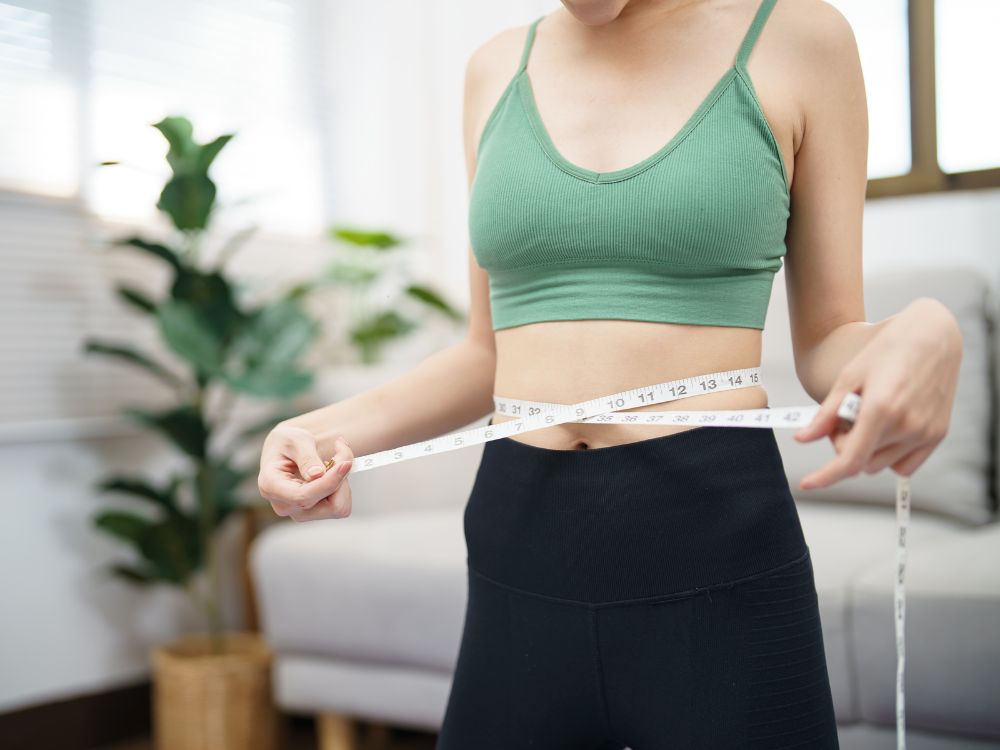 A person measuring their waist with a tape measure.