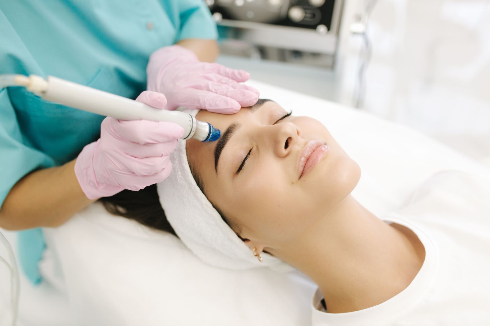 Aesthetician using a facial machine on a female client's face in a clinic, client appears relaxed.