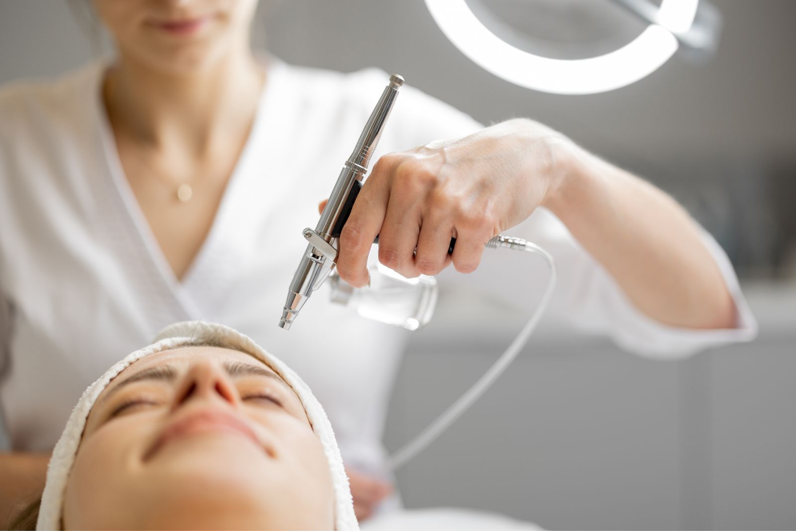 Aesthetician using a microneedling device on a female client's face during a skincare treatment in a well-lit clinic.