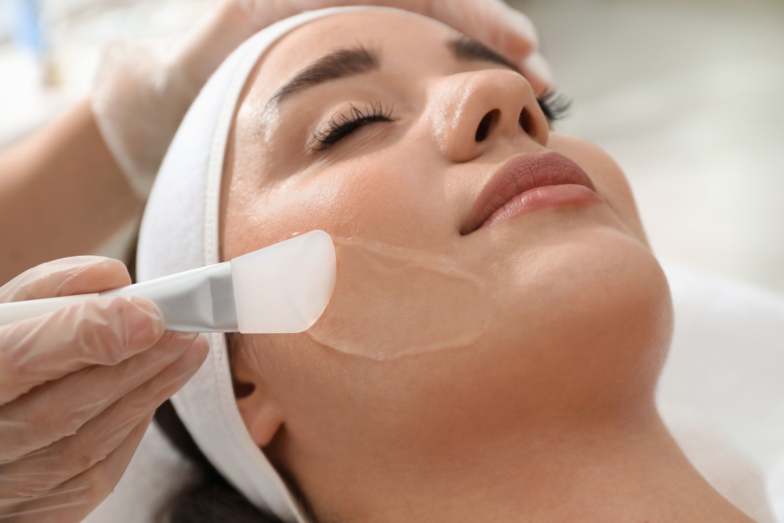 Aesthetician applying a facial mask on a relaxed woman at a spa.