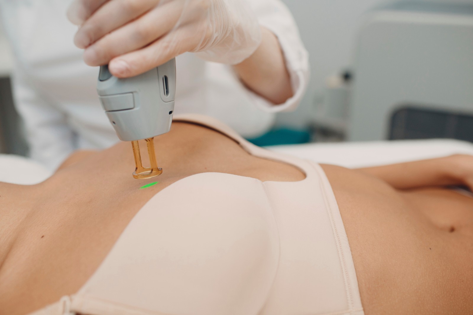 A person undergoing a laser cosmetic procedure on the chest area while wearing a beige bra, with a technician holding the laser device.