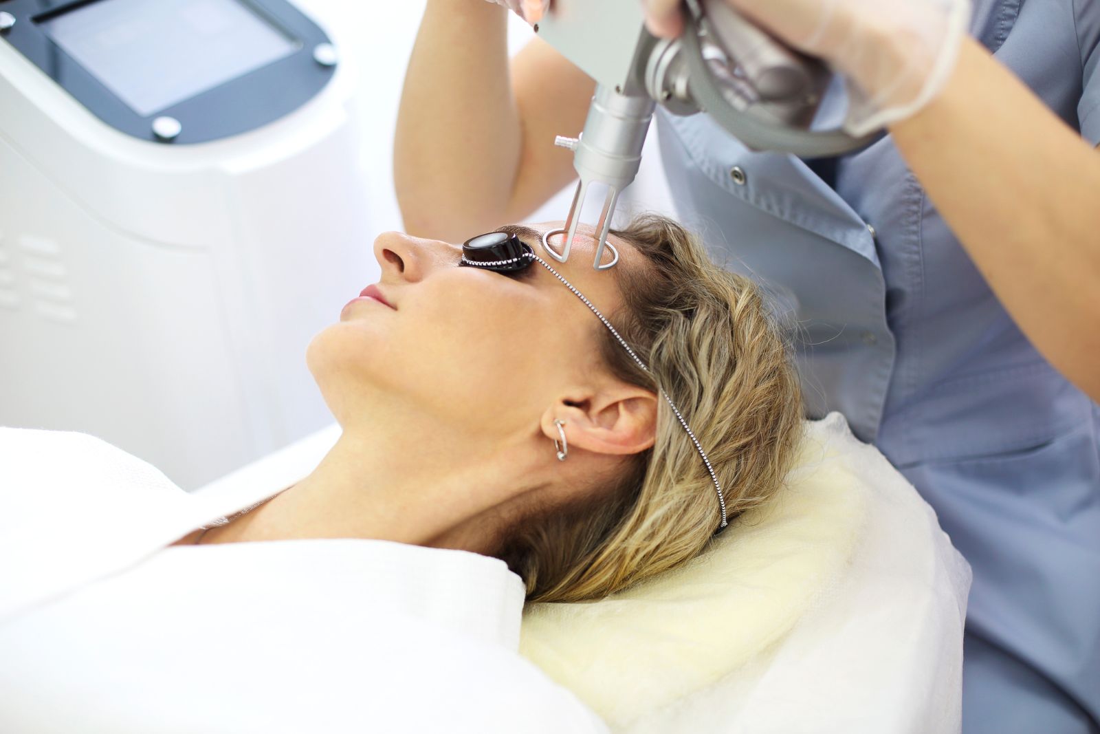 A person undergoing a laser skin resurfacing treatment while lying on a medical chair, wearing protective goggles, as a healthcare professional operates the device.