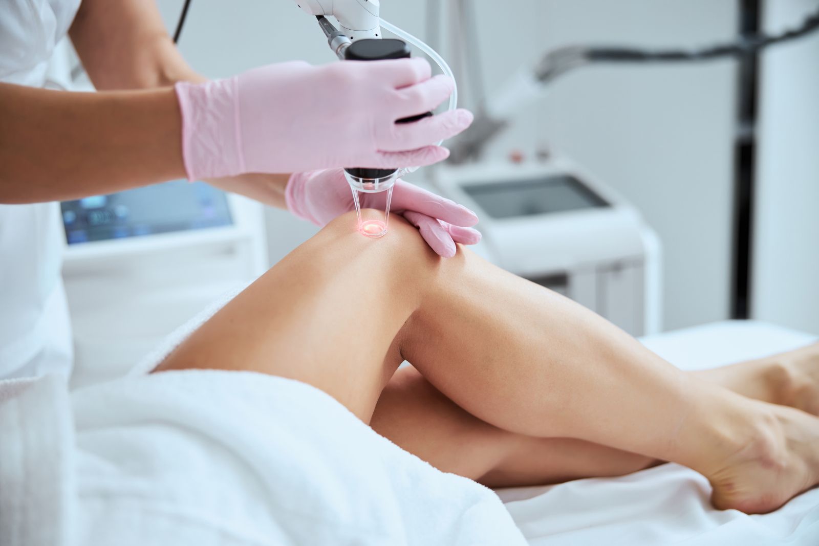 A person wearing pink gloves uses a laser device on another person's leg, possibly performing Laser Vein Therapy, in what appears to be a medical or cosmetic treatment setting.