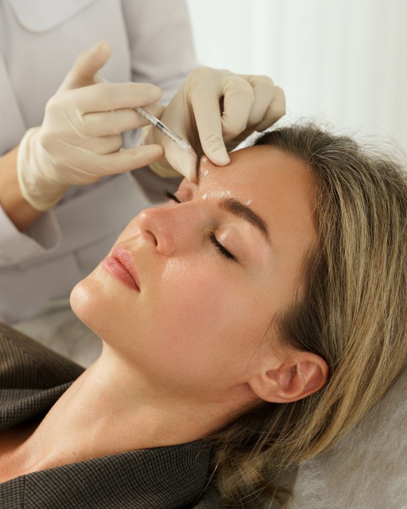 A person in Reno is receiving dermal filler injections in the forehead from someone wearing gloves.