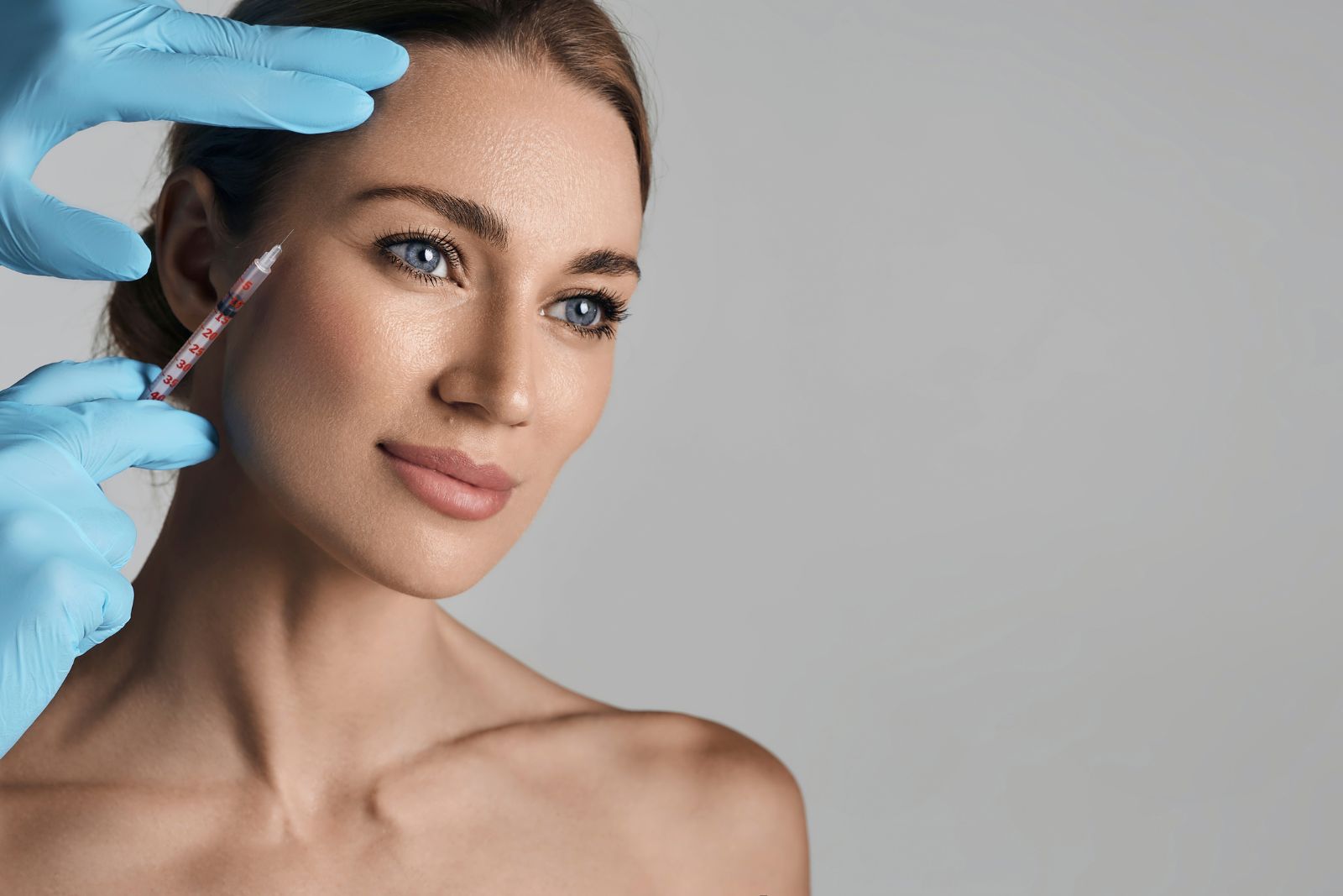 A person with light hair receives a Jeuveau facial injection from someone wearing blue gloves.