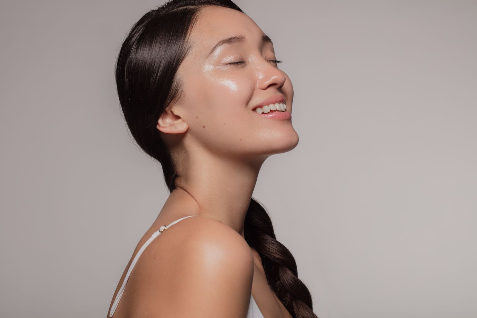 A woman with long, dark hair in a braid, wearing a white top, is smiling with her eyes closed against a plain background, possibly feeling the relief from her recent thyroid injections.