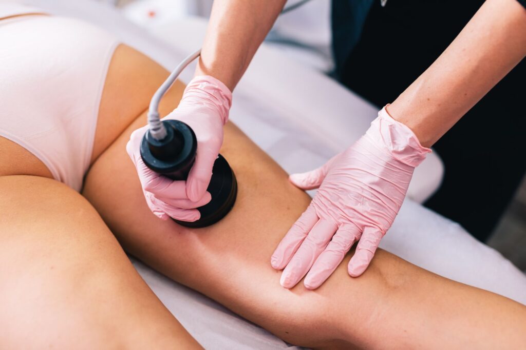 A person in pink gloves uses a handheld device on another person's thigh at an aesthetics med spa in Reno, while the client relaxes on the treatment table.