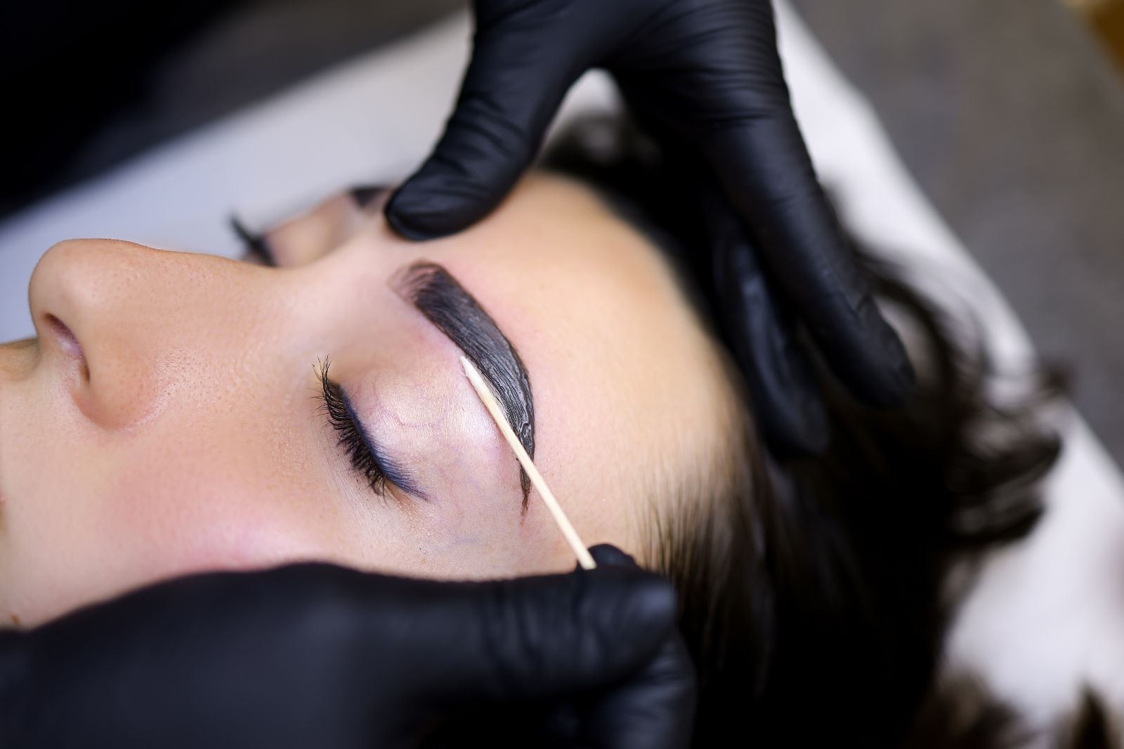 At an aesthetics med spa, a person receives expert eyebrow grooming as gloved hands skillfully shape the brows with a precise stick.