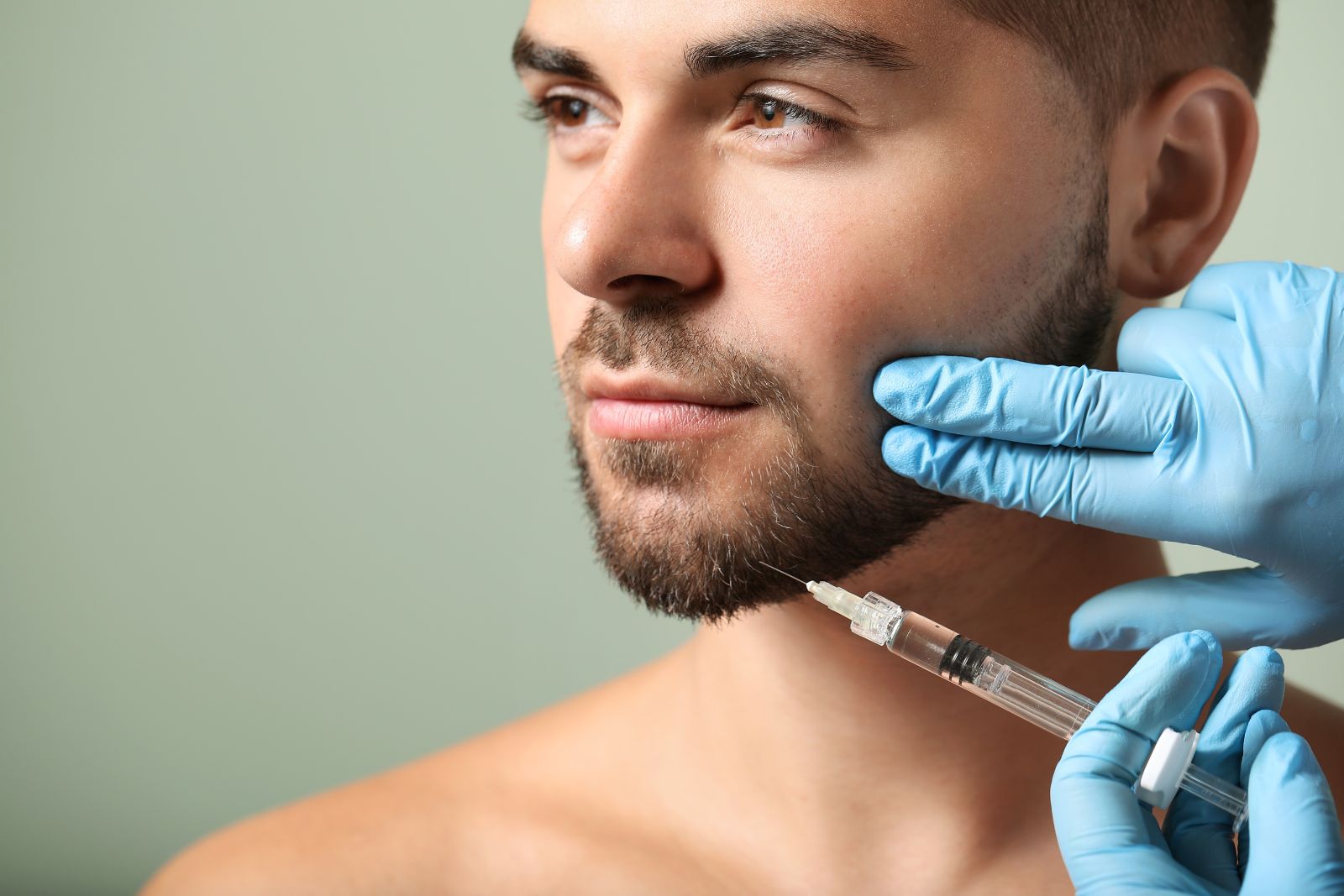 A man with a beard receives an injection in his chin from a gloved hand, showcasing one of the most popular types of dermal fillers.