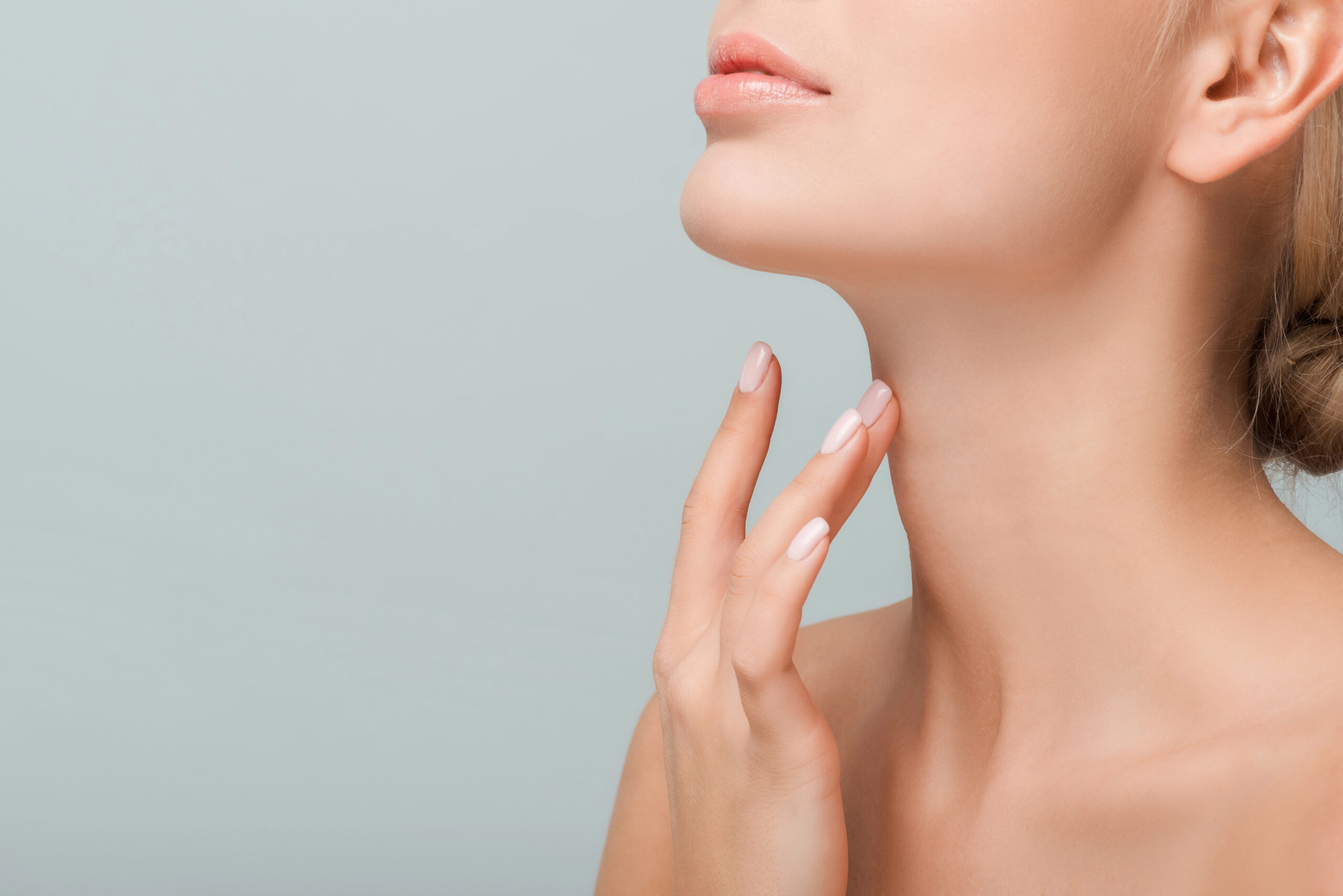 Close-up of a woman's lower face and neck, her hand gently touching her skin, showcases the subtle elegance that PDO threads for neck enhancements can bring, all set against a serene light blue background.