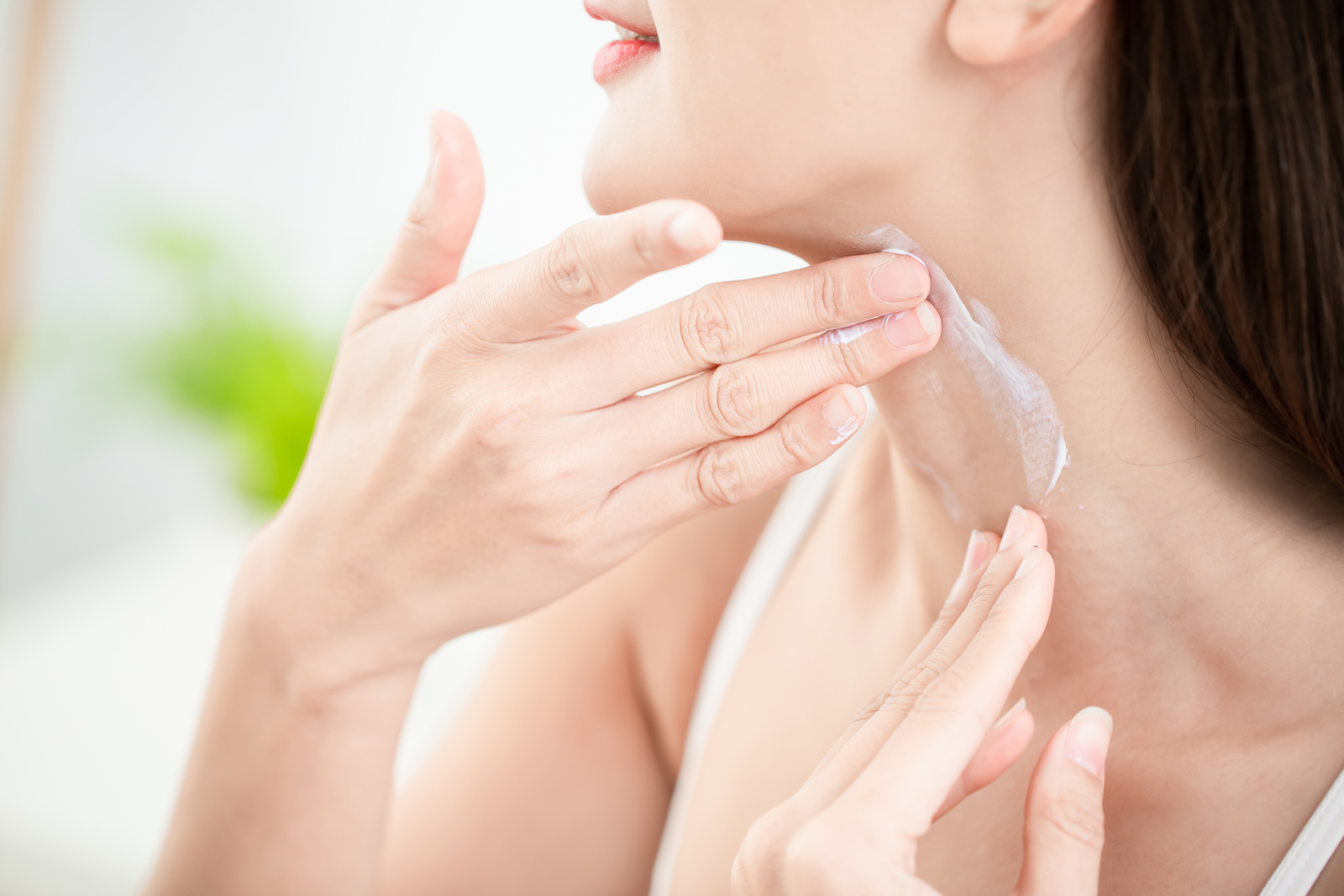 Applying skincare product to their neck with gentle hands, the person contemplates incorporating PDO threads for neck rejuvenation to enhance firmness and achieve a youthful glow.