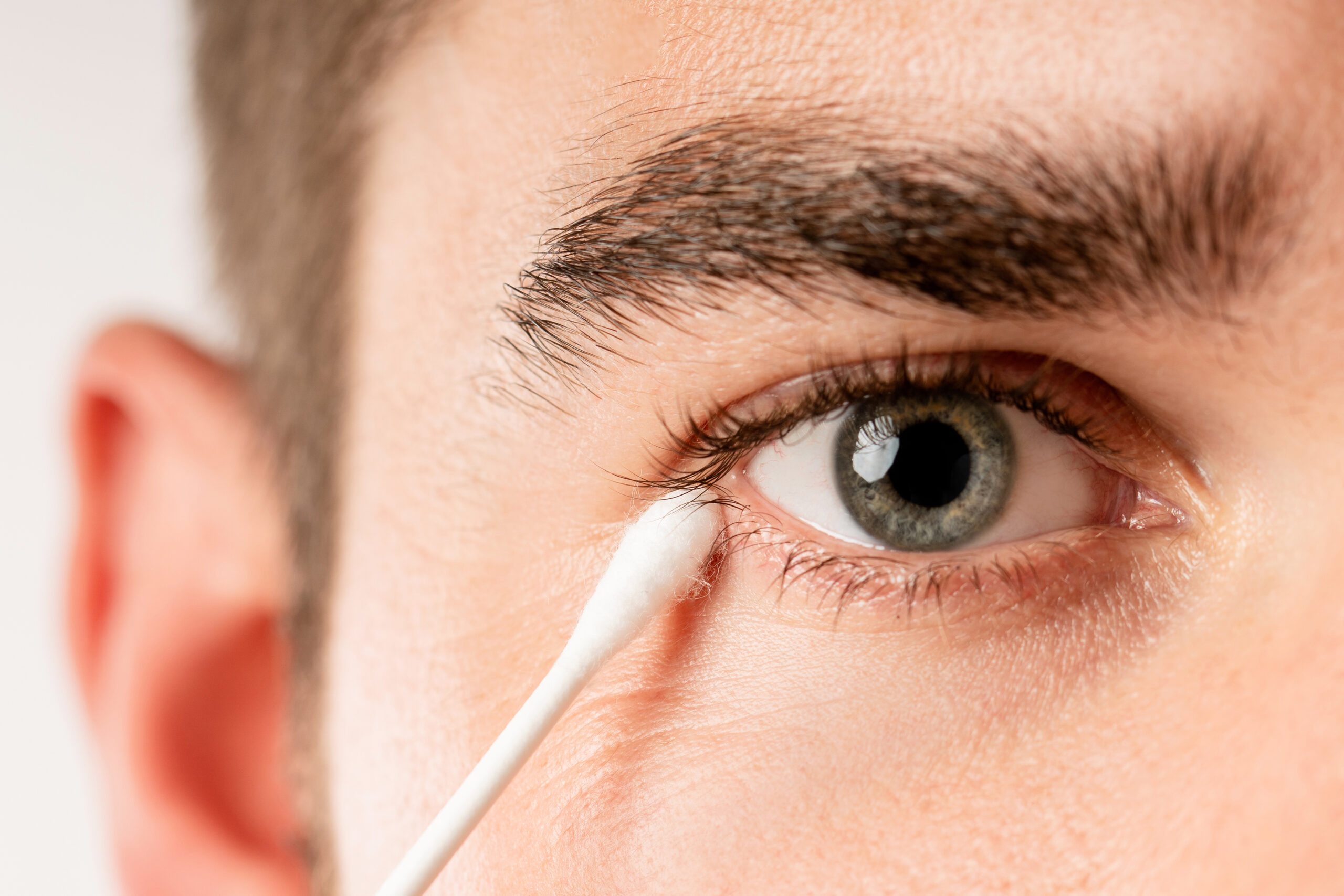 Close-up of a person using a cotton swab to clean the corner of their eye.