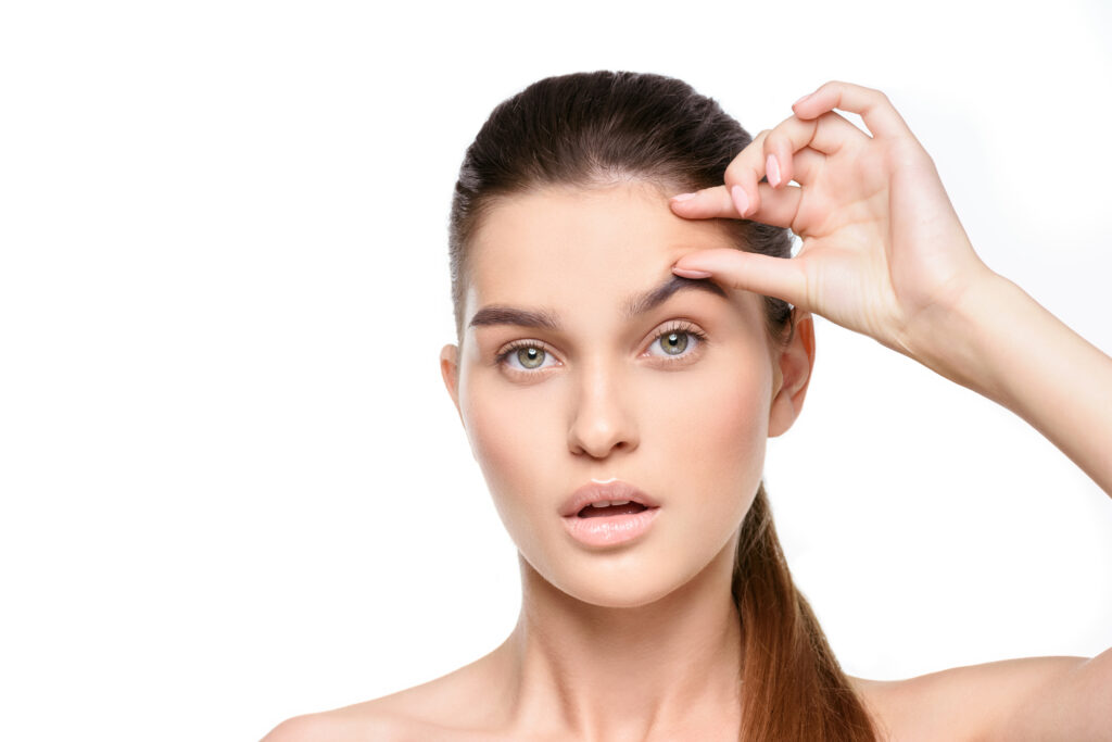 A woman with pulled-back hair holds her fingers to her forehead against a white background, with a neutral expression.