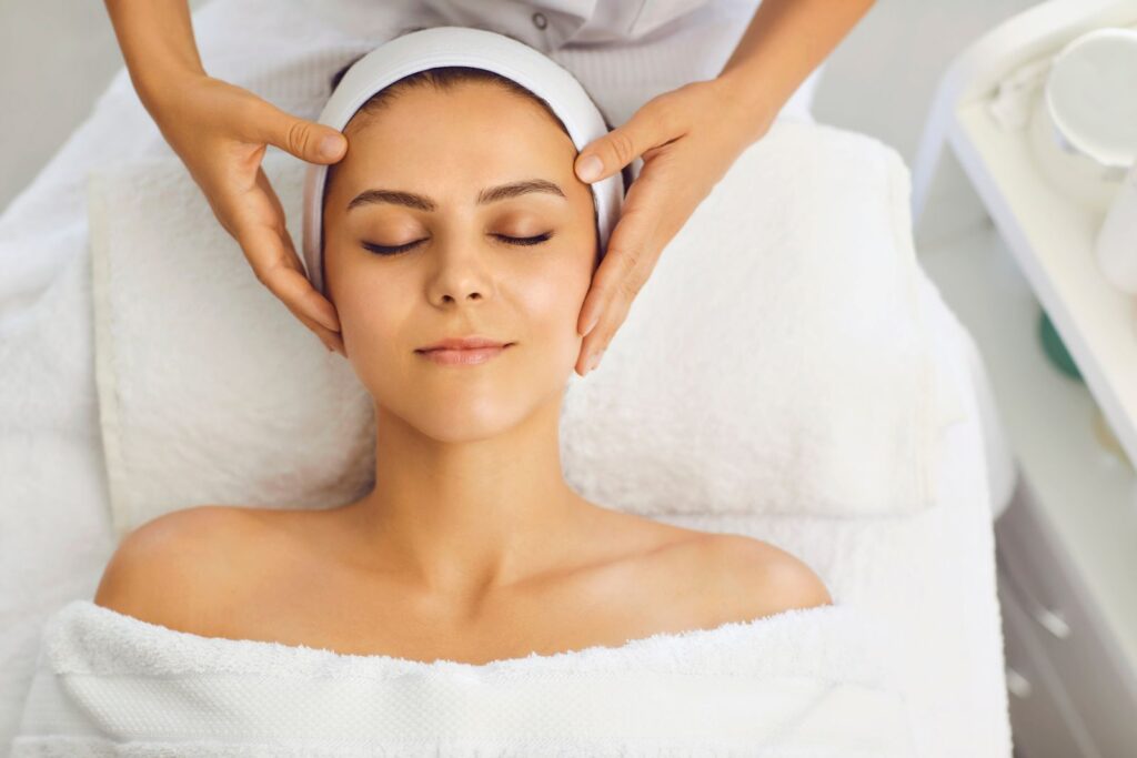 A person with eyes closed, wrapped in a towel, enjoys a soothing facial massage on the treatment table. Alongside such relaxation therapies, understanding what fillers are and exploring types of dermal fillers can enhance your skincare routine and rejuvenate your appearance.