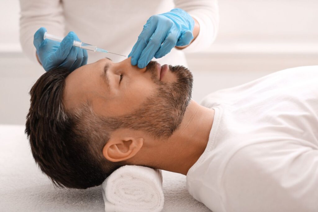 A person lying down receives a cosmetic injection in the nose area from a professional wearing blue gloves.