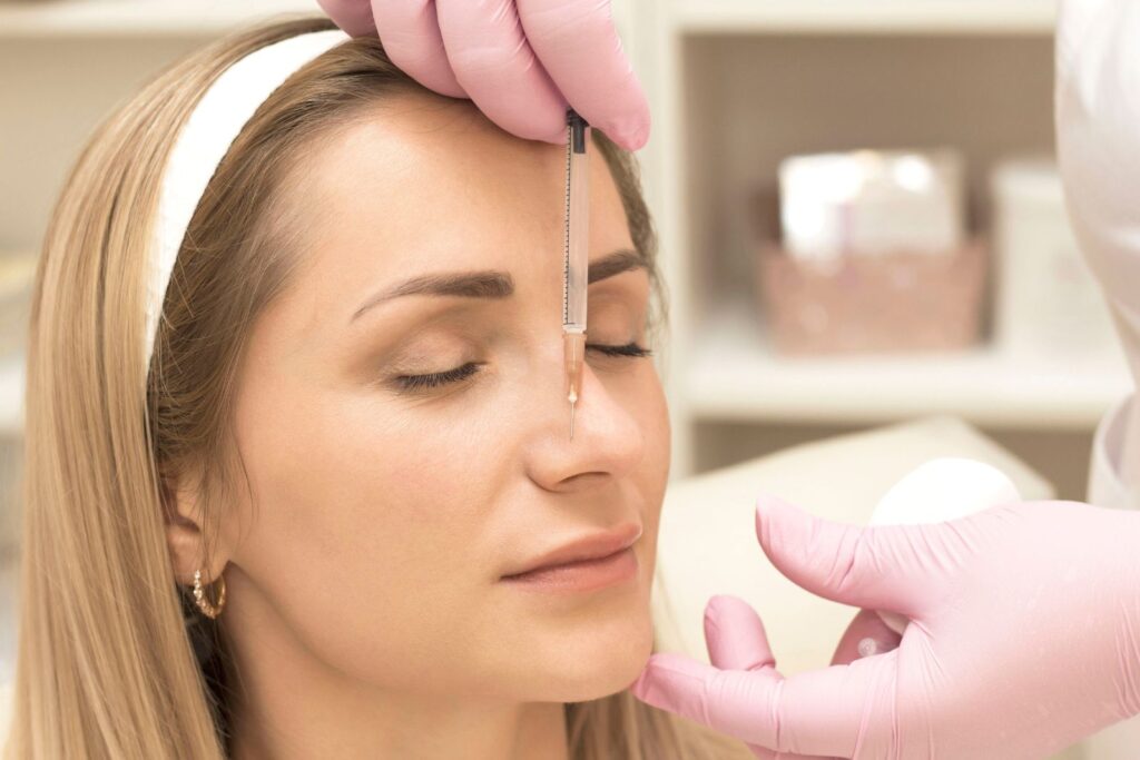 A person receiving a cosmetic facial injection, administered by someone wearing pink gloves.