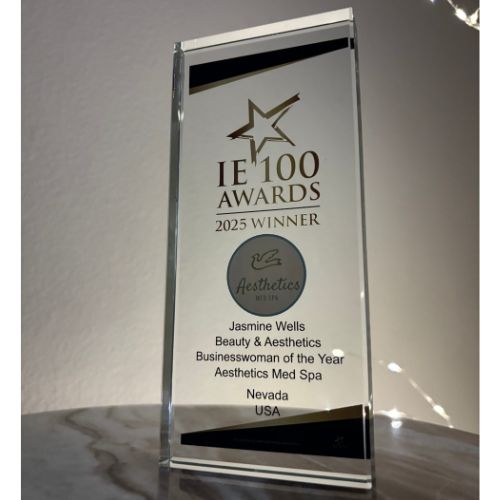 A glass award engraved with "IE 100 Awards 2025 Winner" and presented to Jasmine Wells for Beauty & Aesthetics Businesswoman of the Year, recognizing Aesthetics Med Spa as Reno's Best Med Spa, Nevada, USA.
