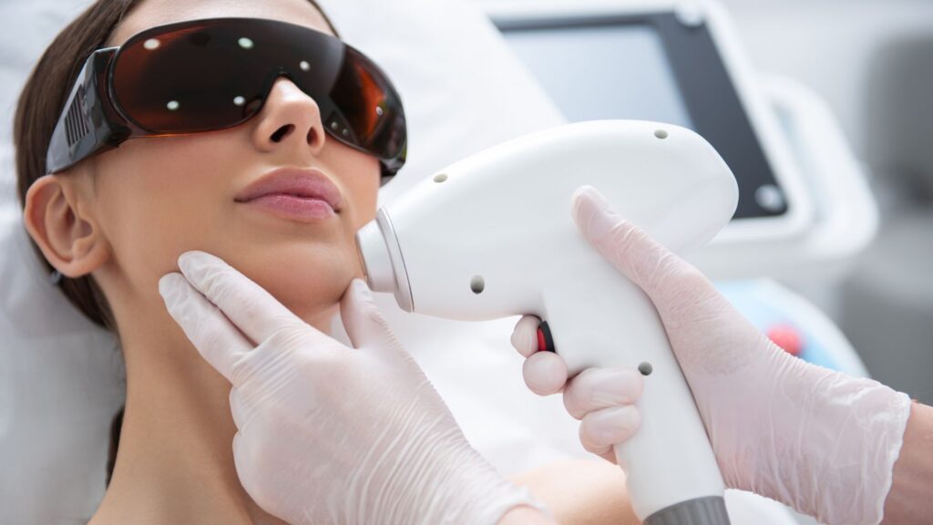 A person wearing protective eyewear receives a laser skin treatment on the face from a professional wearing gloves, in a clinical med spa setting offering advanced medical services.