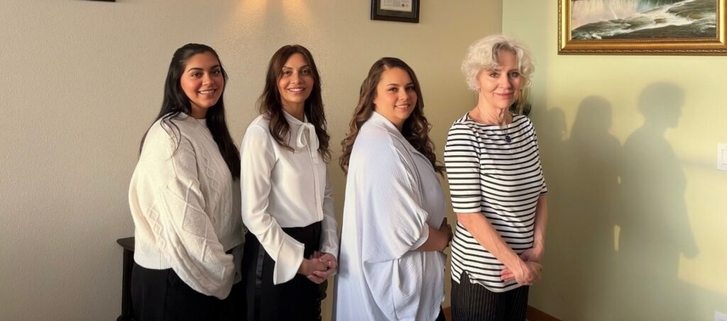 Four women stand indoors in a row at Aesthetics Medspa in Reno, facing the camera and smiling. The background includes framed artwork and a light-colored wall, reflecting the welcoming atmosphere of this Medical Spa.