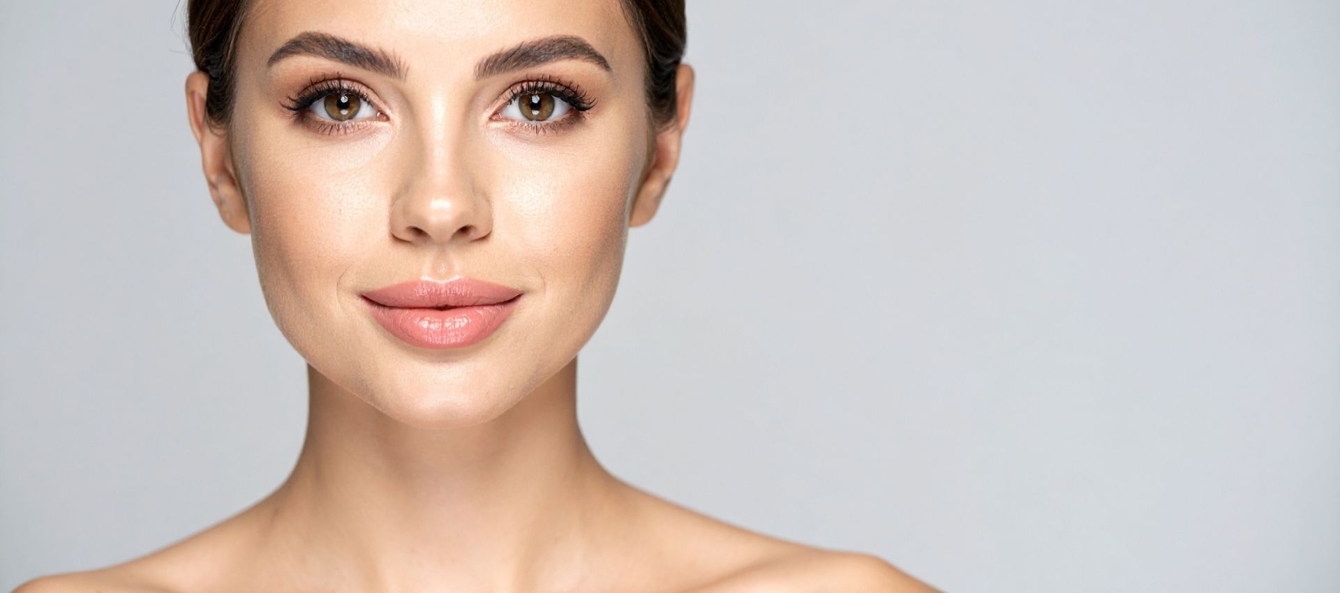 Woman with smooth skin and natural makeup looks directly at the camera against a plain light background, shoulders bare—a radiant confidence that could be attributed to healthy lifestyle choices, including options like tirzepatide injections.