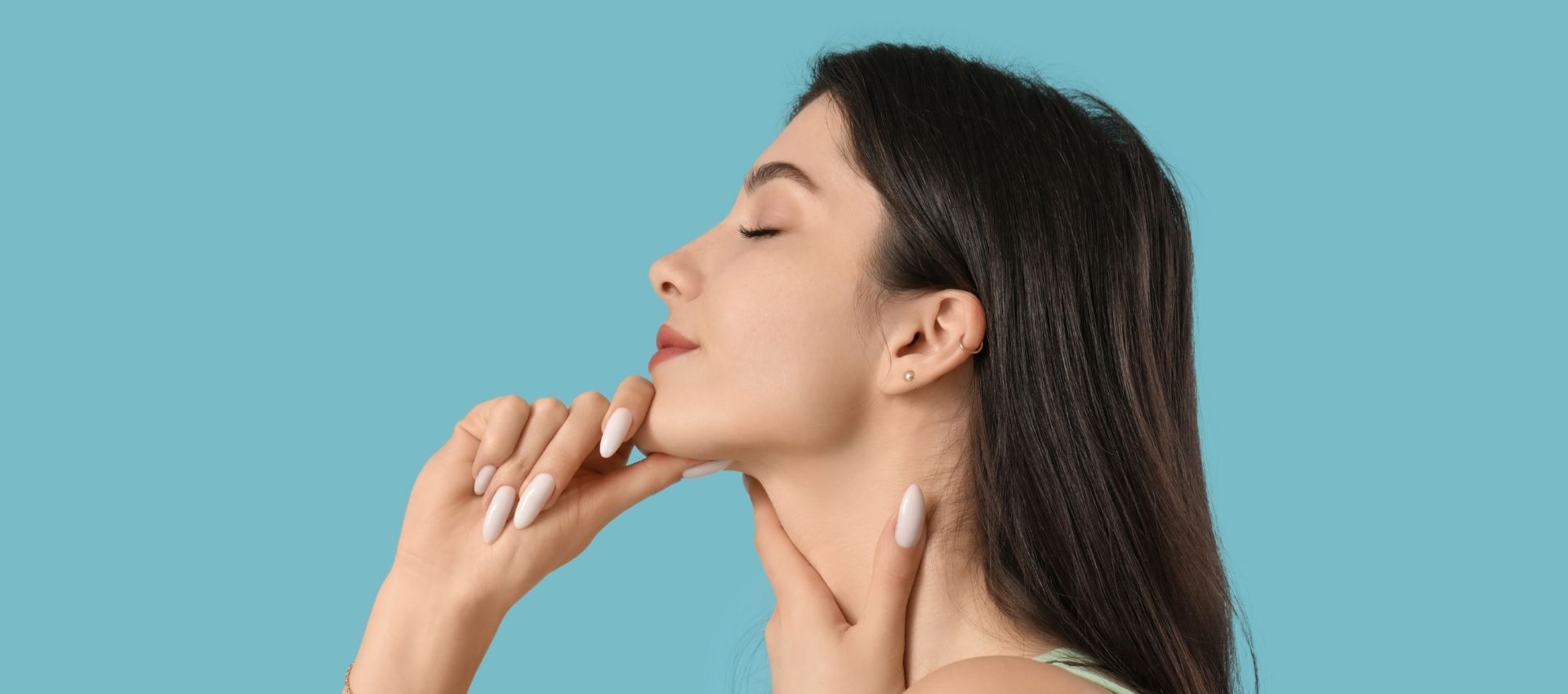 Woman in profile with eyes closed, touching her chin and neck with both hands, against a solid light blue background—perfectly capturing the elegance often sought after with dermal filler for jawline enhancement.