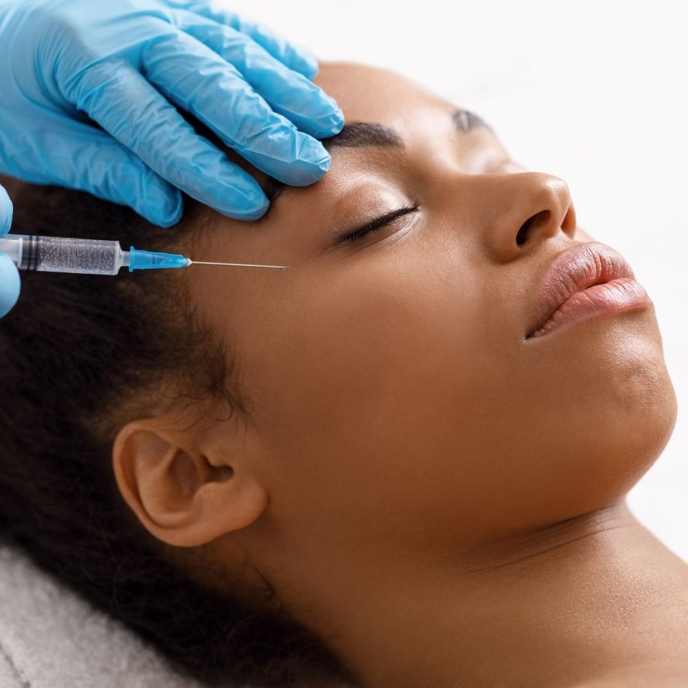 A person with closed eyes receives a facial injection near the eye area from a gloved healthcare worker, demonstrating the careful application of derma filler for under eyes.