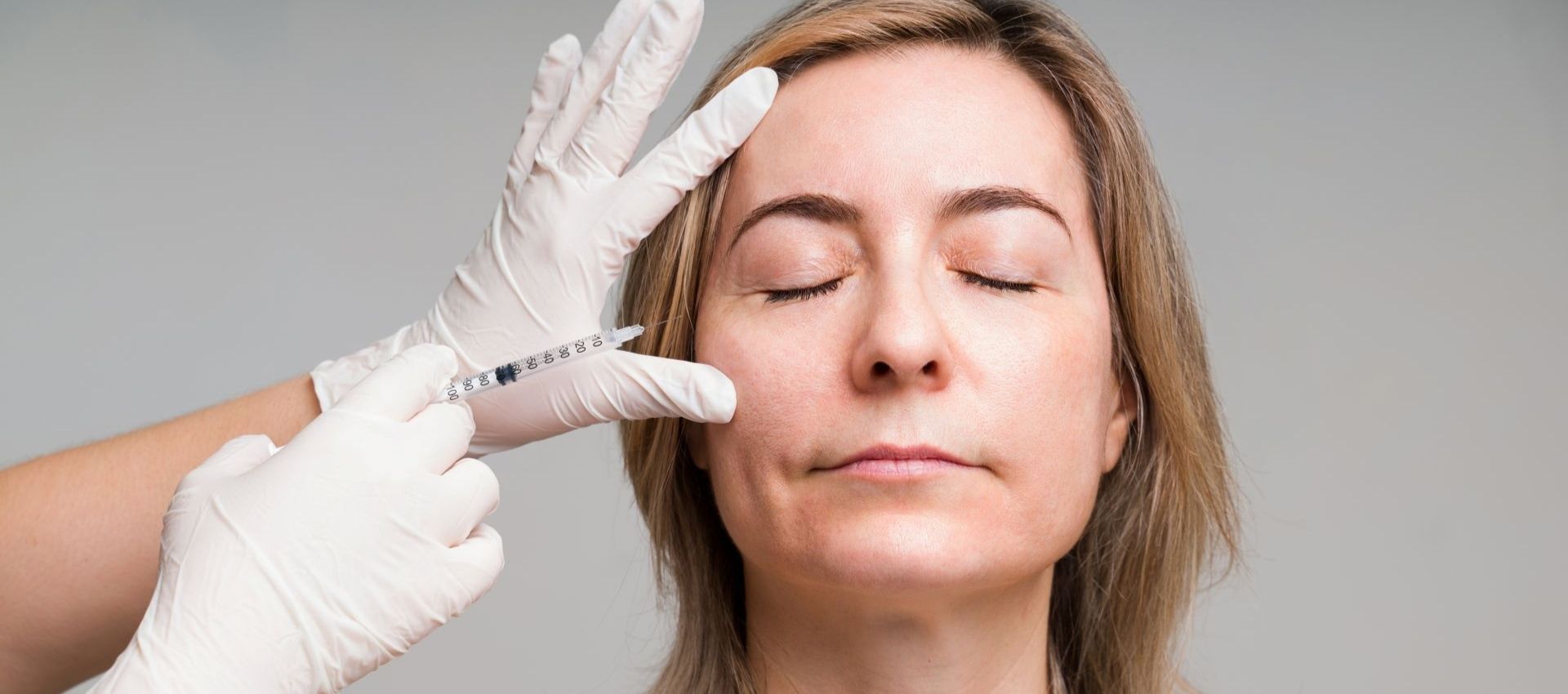 A person with closed eyes receives a facial injection from a gloved hand, addressing volume loss temples with a derma filler for temples.